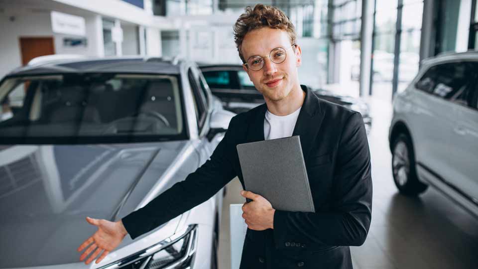 Ein Verkäufer zeigt auf ein Auto und erklärt dem Kunden die Konditionen beim Auto verkaufen Konstanz